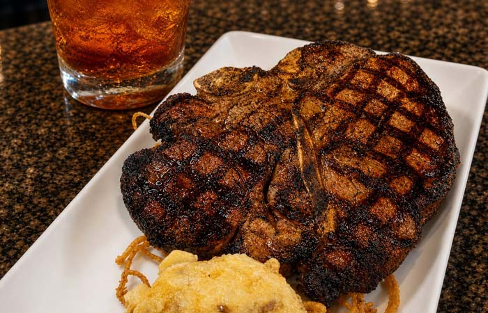 Grilled steak with char marks, plus seafood or cocktails, served on a white plate with sides.