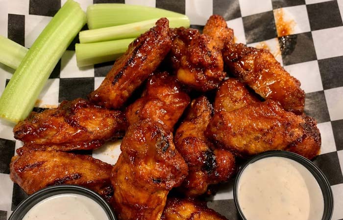Buffalo wings, ranch, celery, and cocktails at Torey’s Restaurant & Bar on checkered paper.