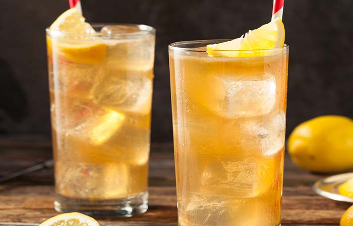 Two glasses of iced tea with lemon wedges and red-striped straws on a wooden steakhouse table.