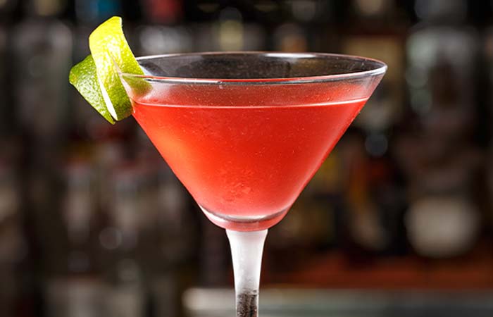 Red cocktail in a martini glass at Torey’s Restaurant & Bar, garnished with two lime wedges.