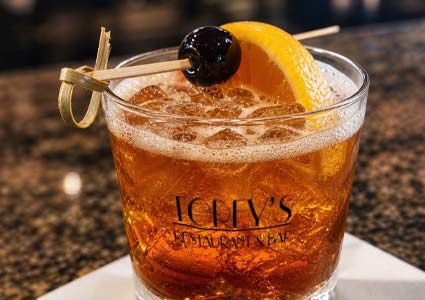 Cocktails with orange slice and cherry garnish on ice, served in a glass on a white napkin.
