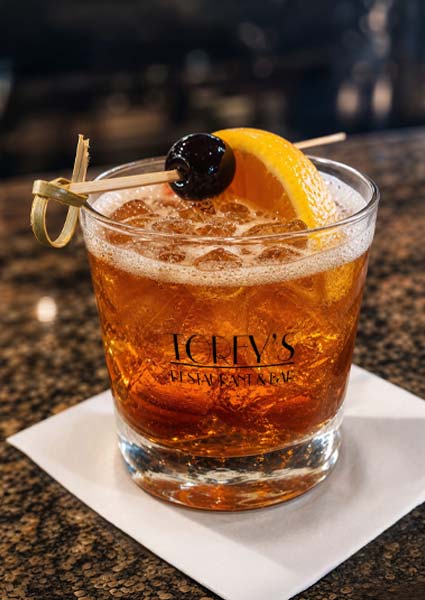 Old fashioned cocktail garnished with orange and cherry at Torey’s Restaurant & Bar on a napkin.